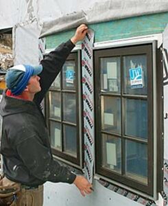 A person in Markham applies flashing tape around the frame of a newly installed window on a building under construction.