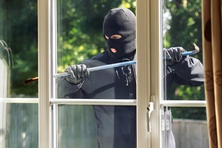 A person wearing a ski mask and gloves stands outside a Markham window holding a crowbar, appearing to attempt a break-in.