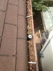 A house gutter in Markham filled with leaves and debris, with a drain cover visible in the middle, viewed from the roof’s edge.