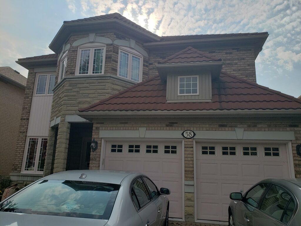 Two silver cars parked in front of a Markham two-story house with brick and stone exterior, red-tiled roof, and double garage doors under a partly cloudy sky.