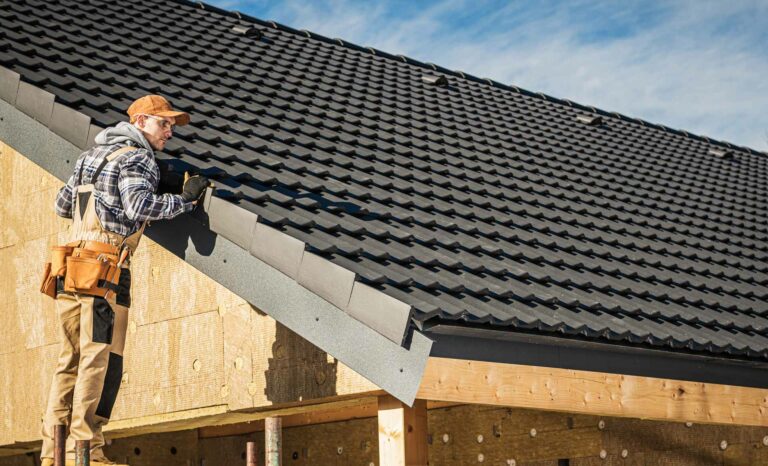 A construction worker in Markham, wearing a cap and tool belt, installs black roof tiles on a partially finished wooden building.
