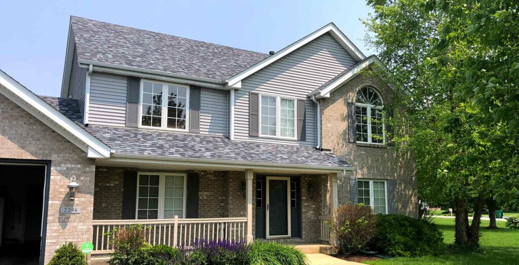 Two-story suburban Markham house with gray siding, brick accents, white trim, and a covered front porch, surrounded by green lawn and trees.