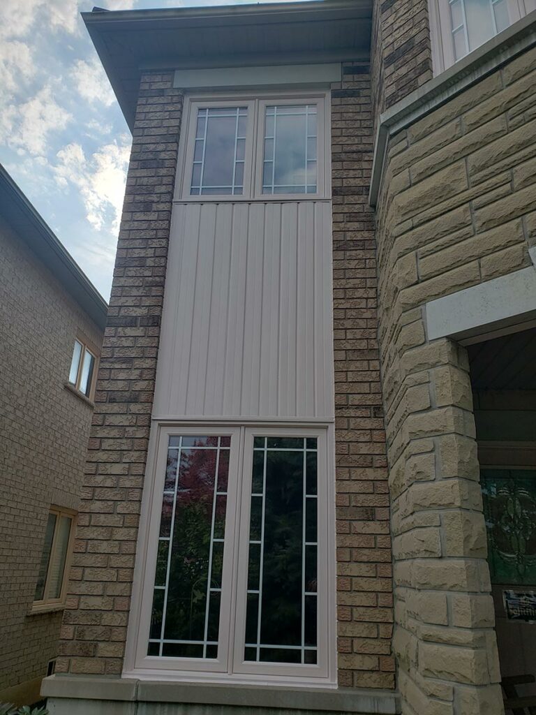 A two-story brick and stone house facade in Markham with four large windows featuring grid patterns, set against a partly cloudy sky.