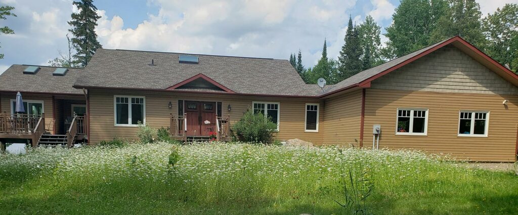 Single-story house with a gabled roof surrounded by trees in Markham, featuring a wildflower-filled front yard under a partly cloudy sky.