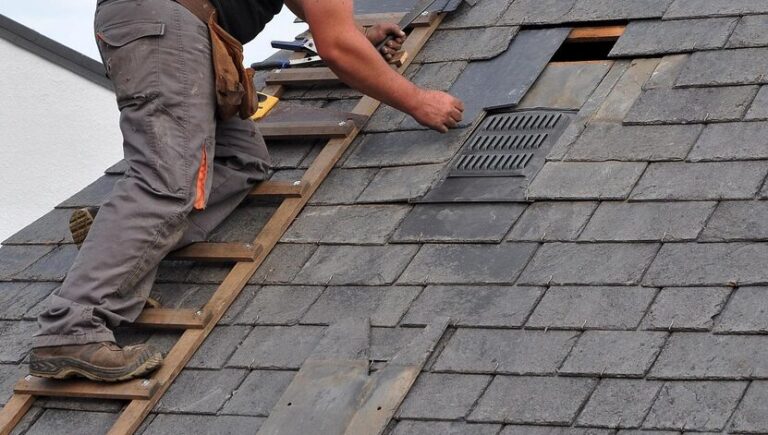 roofer standing on a roof ladder installing shingles
